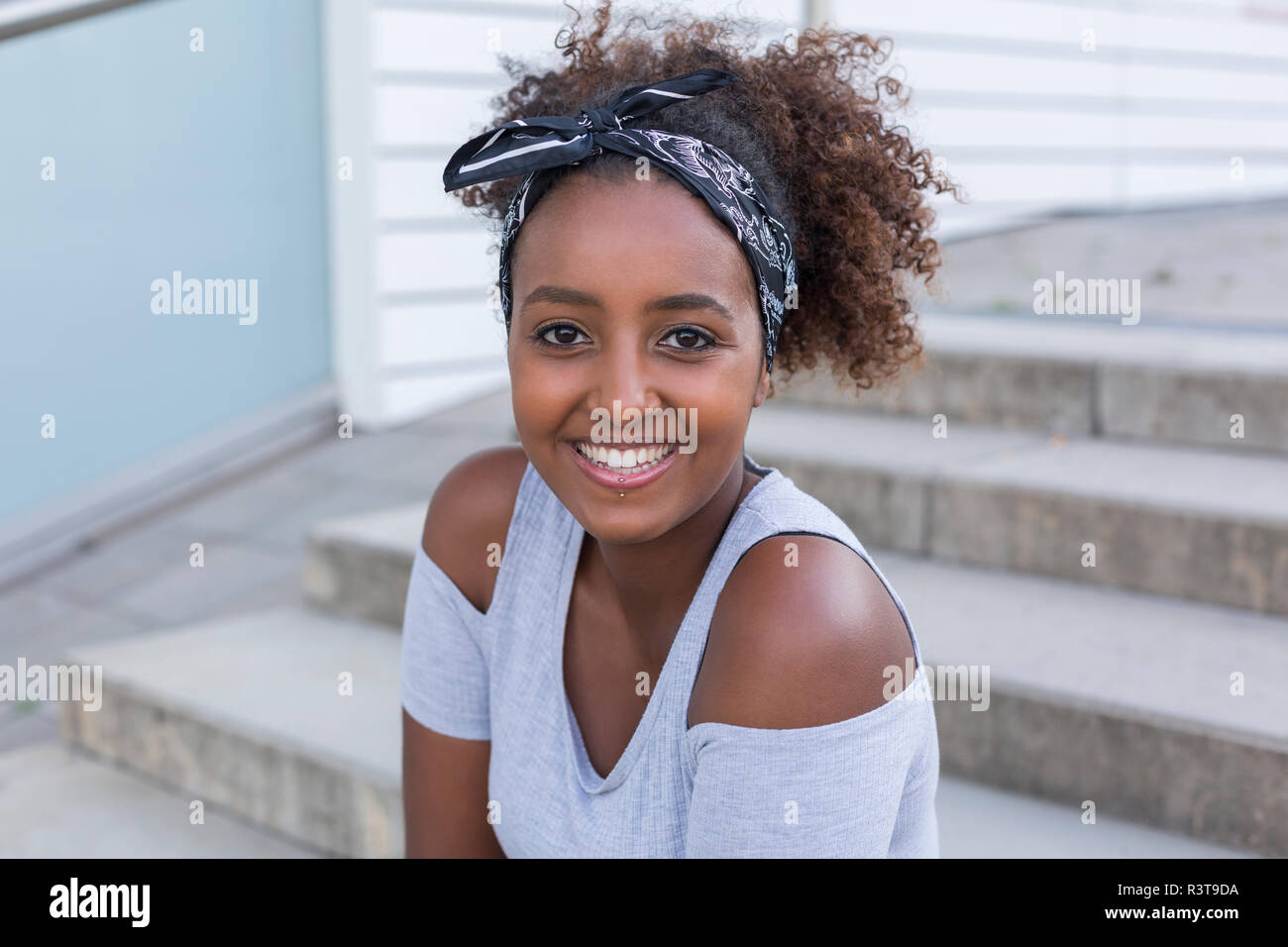 Ritratto di sorridente giovane donna indossa fascia per capelli seduti sulle scale Foto Stock