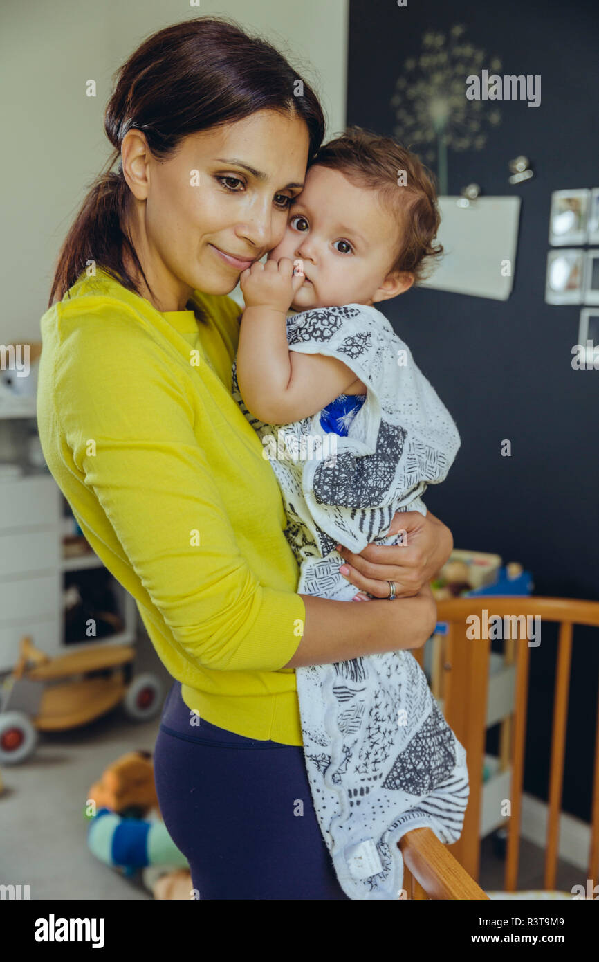 Sorridente madre tenendo il suo bambino in sacco a pelo in Camera bambino Foto Stock