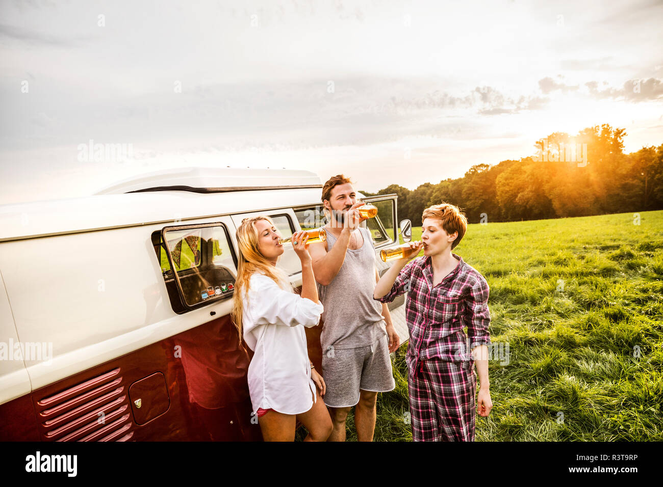 Amici in pigiama bevendo birra in un furgone nel paesaggio rurale Foto Stock