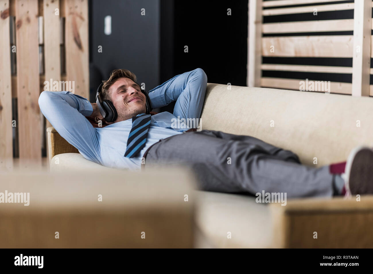 Imprenditore con le cuffie sdraiato sul lettino nella sala di office Foto Stock