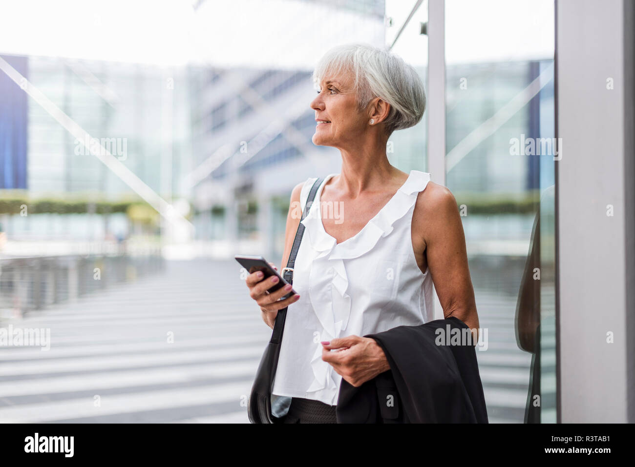 Donna senior con un telefono cellulare nella città guardando intorno Foto Stock