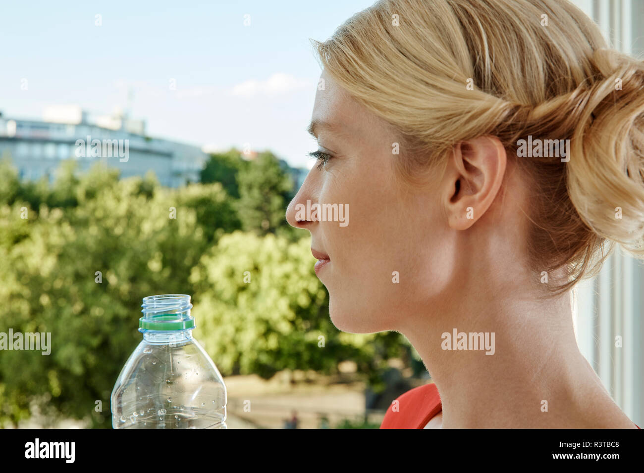 Giovane donna con bottiglia di acqua guardando fuori dalla finestra Foto Stock