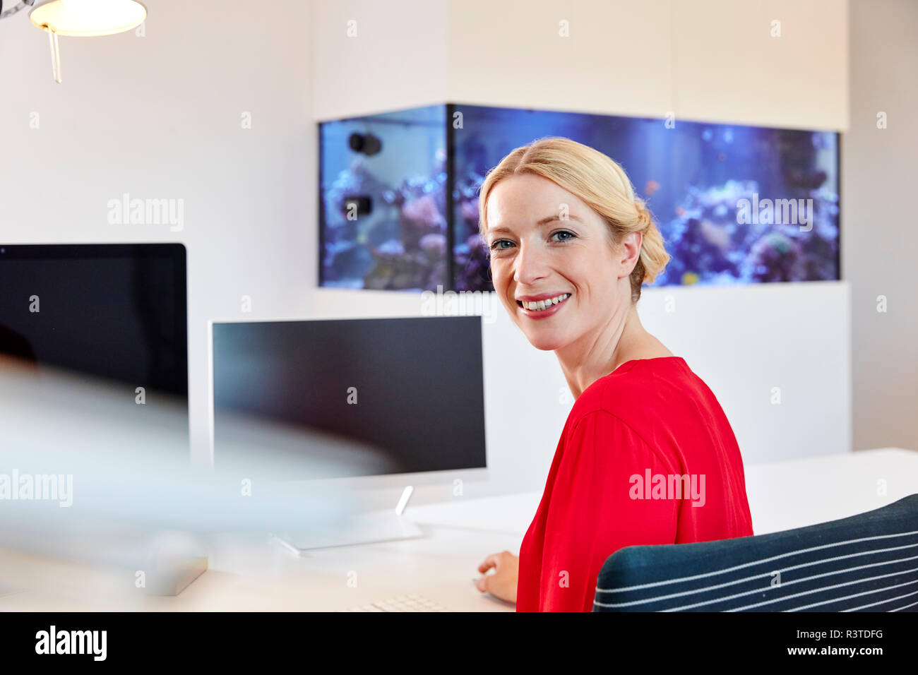 Ritratto di sorridente giovane donna seduta alla scrivania in ufficio Foto Stock