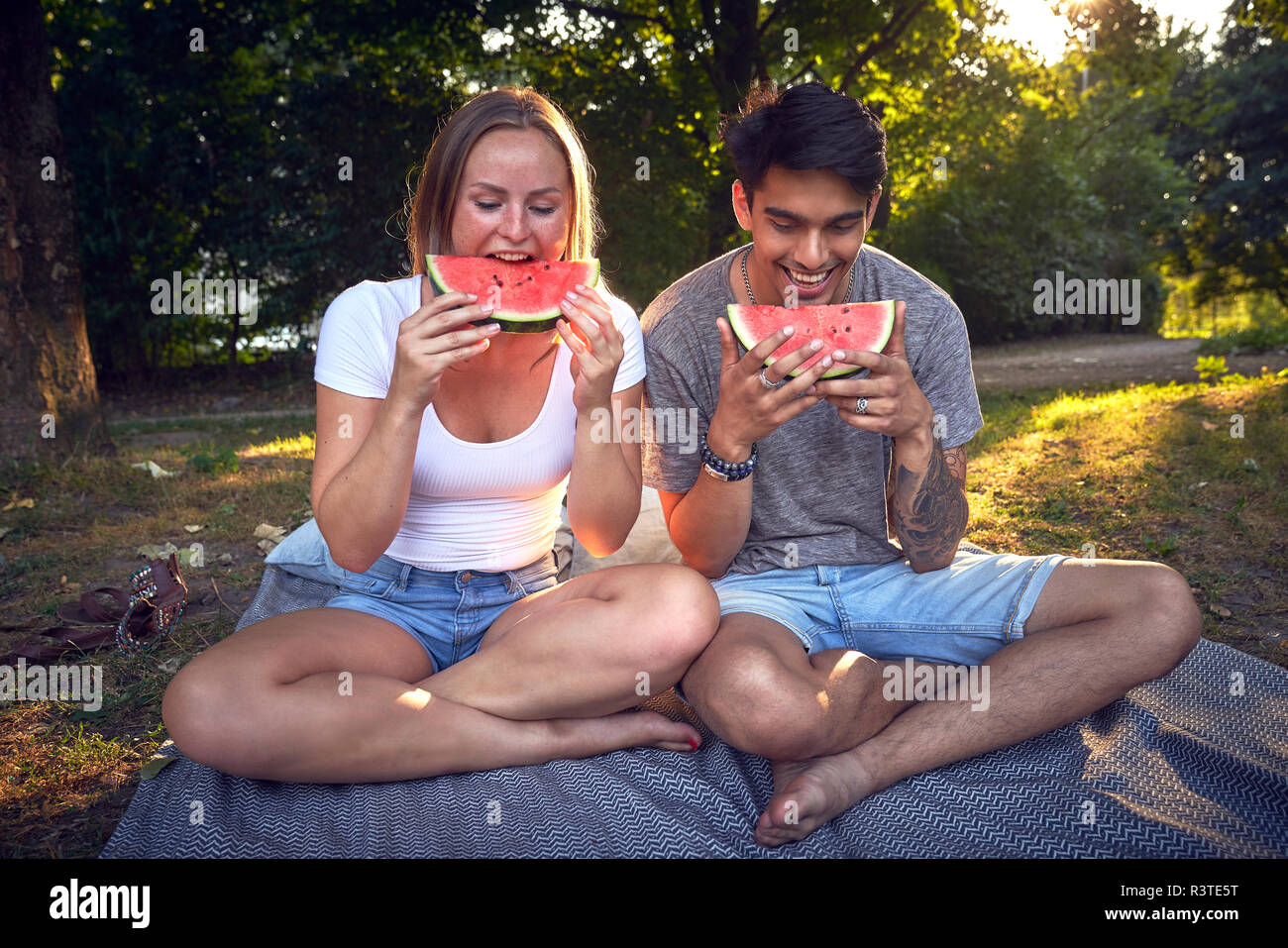 Coppia giovane seduto nel parco, mangiando anguria Foto Stock