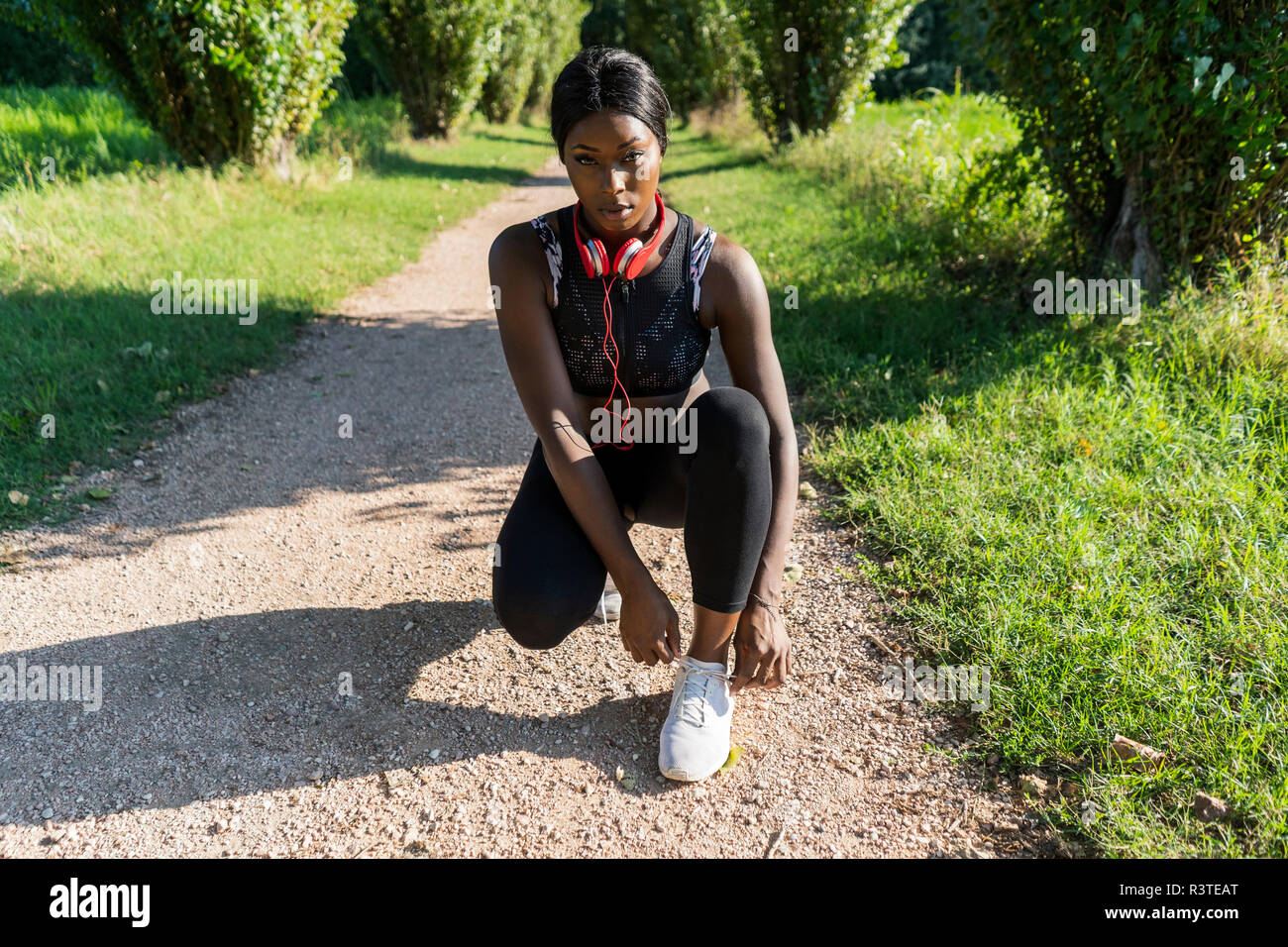Giovane atleta accovacciato su sterrato, scarpe di legatura Foto Stock
