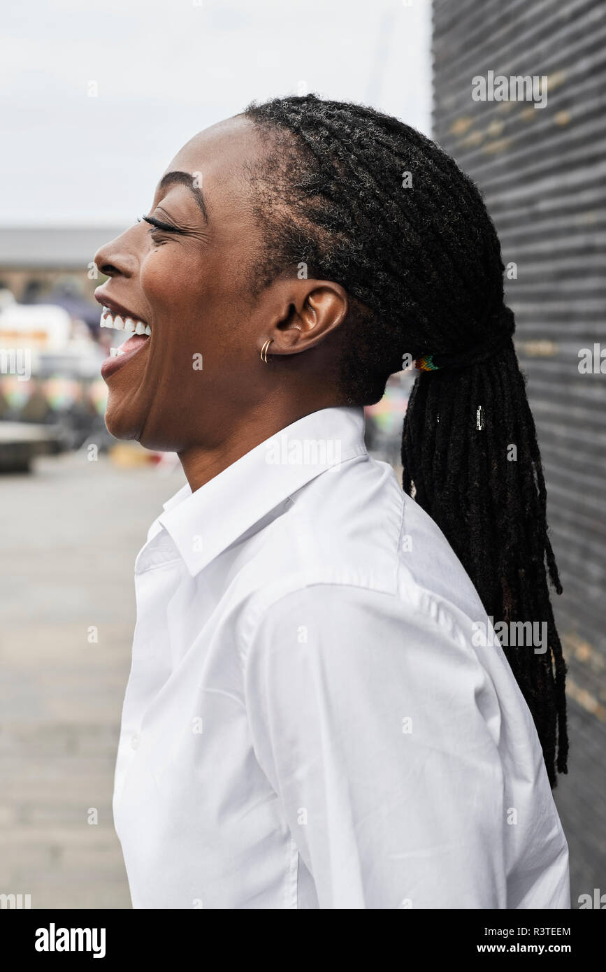 Profilo di ridere imprenditrice con dreadlocks che indossa una camicia bianca Foto Stock