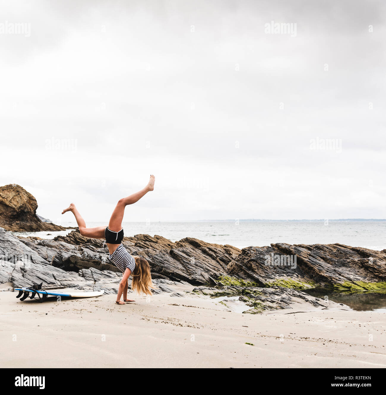 Giovane donna con la tavola da surf facendo handstand sulla spiaggia Foto Stock