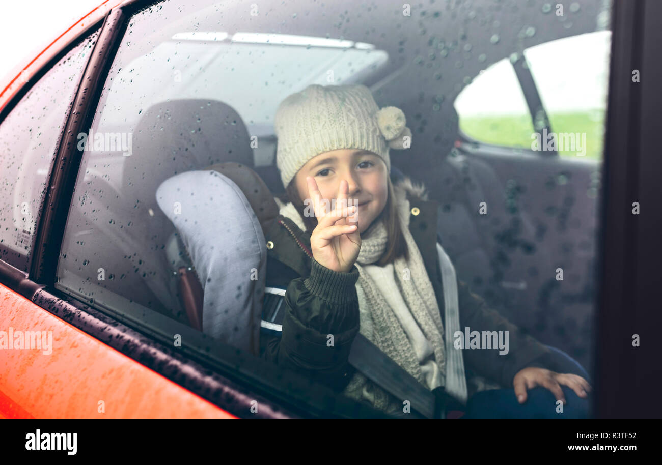 Ritratto di felice bambina con cappello di lana facendo segno di vittoria mentre si viaggia in auto Foto Stock