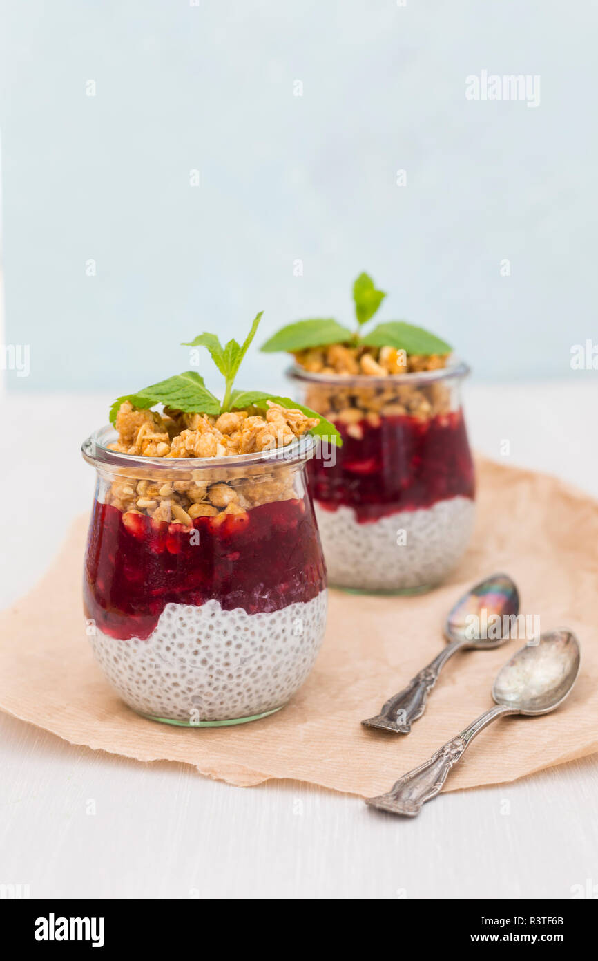 Due bicchieri di chia il budino con latte di cocco, gelatine di frutti rossi e arachide granola topping Foto Stock