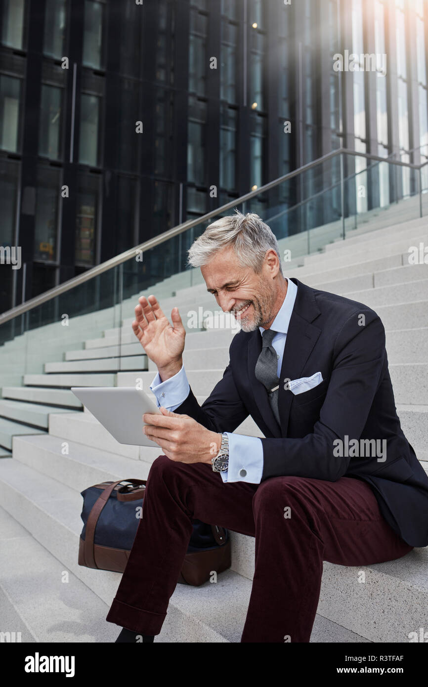 Moda uomo d affari con borsa da viaggio seduti sulle scale utilizzando tablet Foto Stock