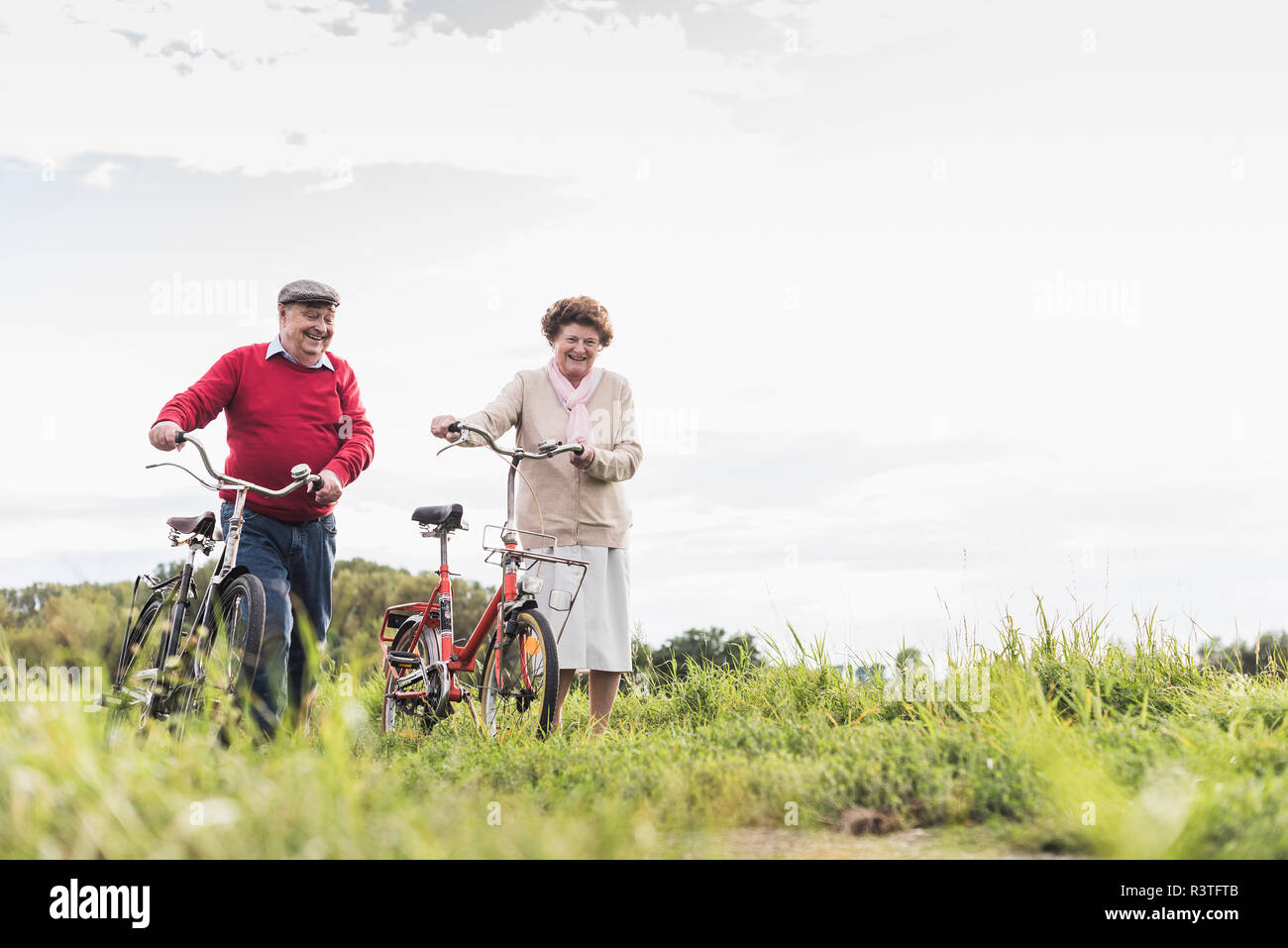 Coppia senior spingendo le biciclette nel paesaggio rurale Foto Stock