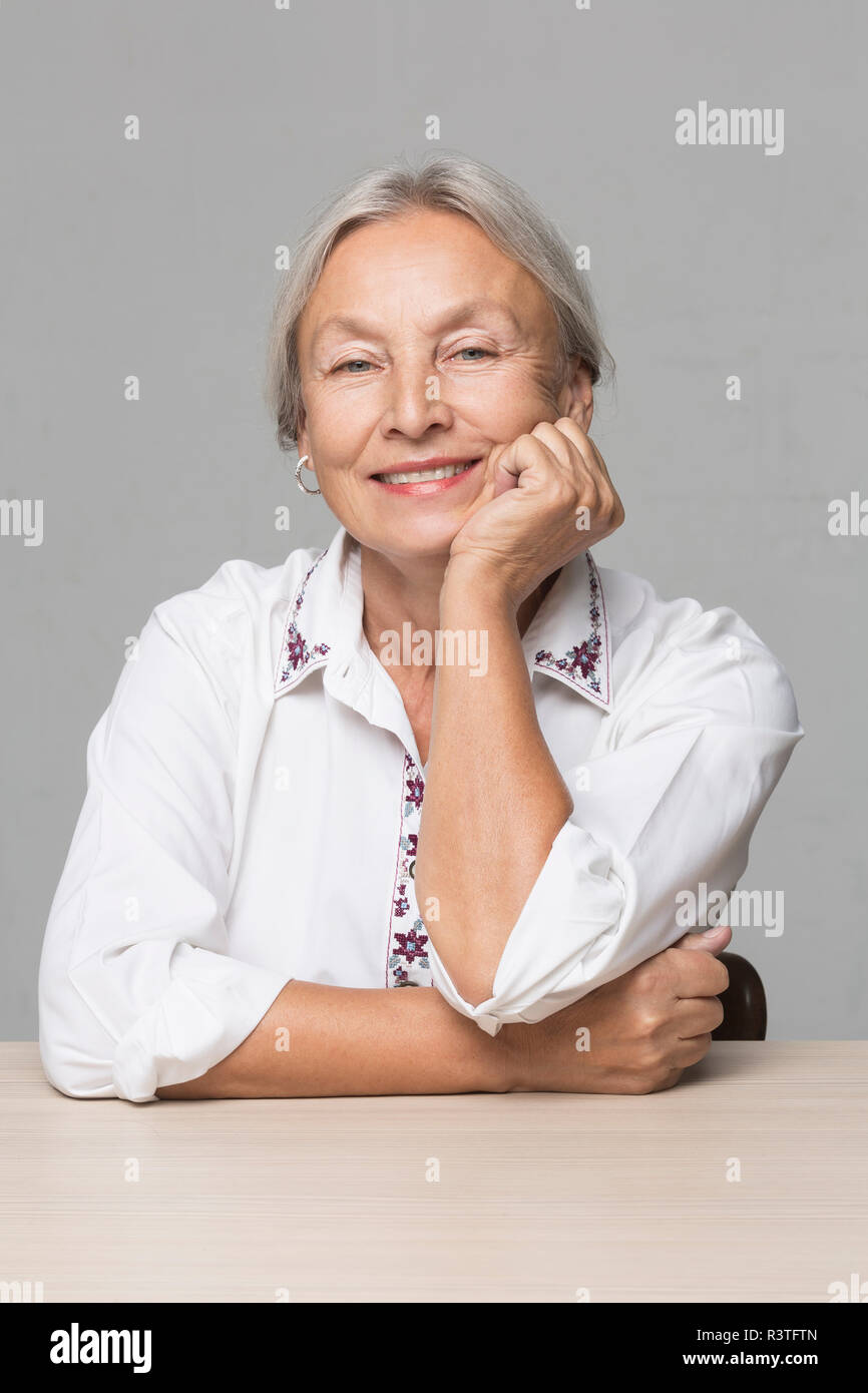 Ritratto di donna senior con i capelli grigi seduta a tavola con testa in mano Foto Stock