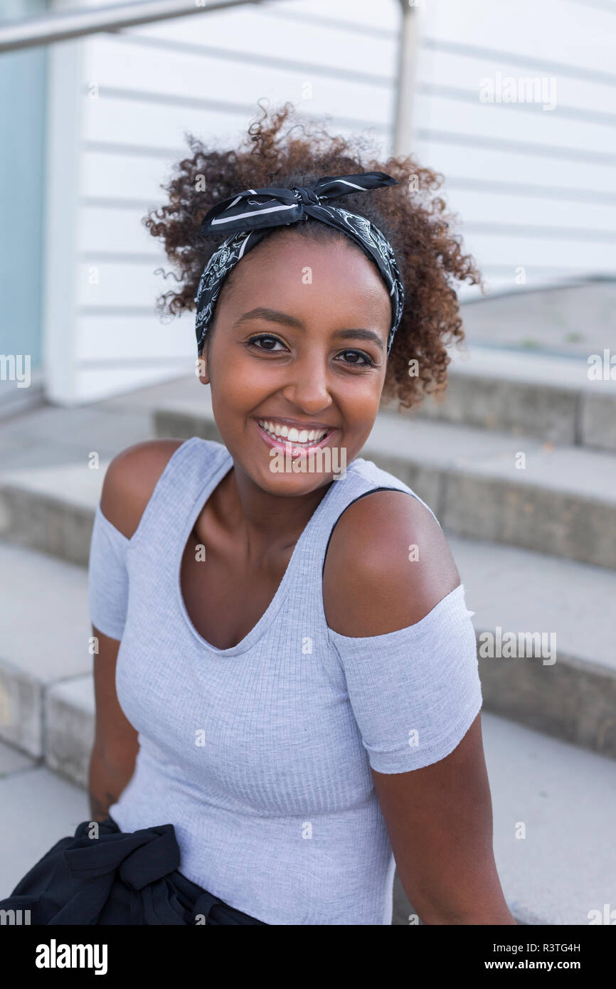 Ritratto di felice giovane donna con fascia per capelli seduti sulle scale Foto Stock