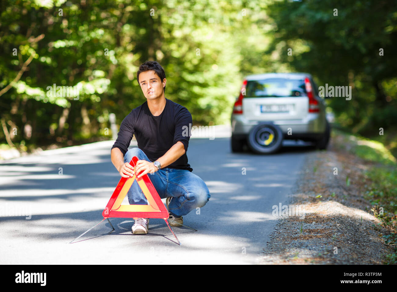 Bel giovane uomo con la sua vettura ripartiti per la strada, l'impostazione del triangolo di sicurezza Foto Stock