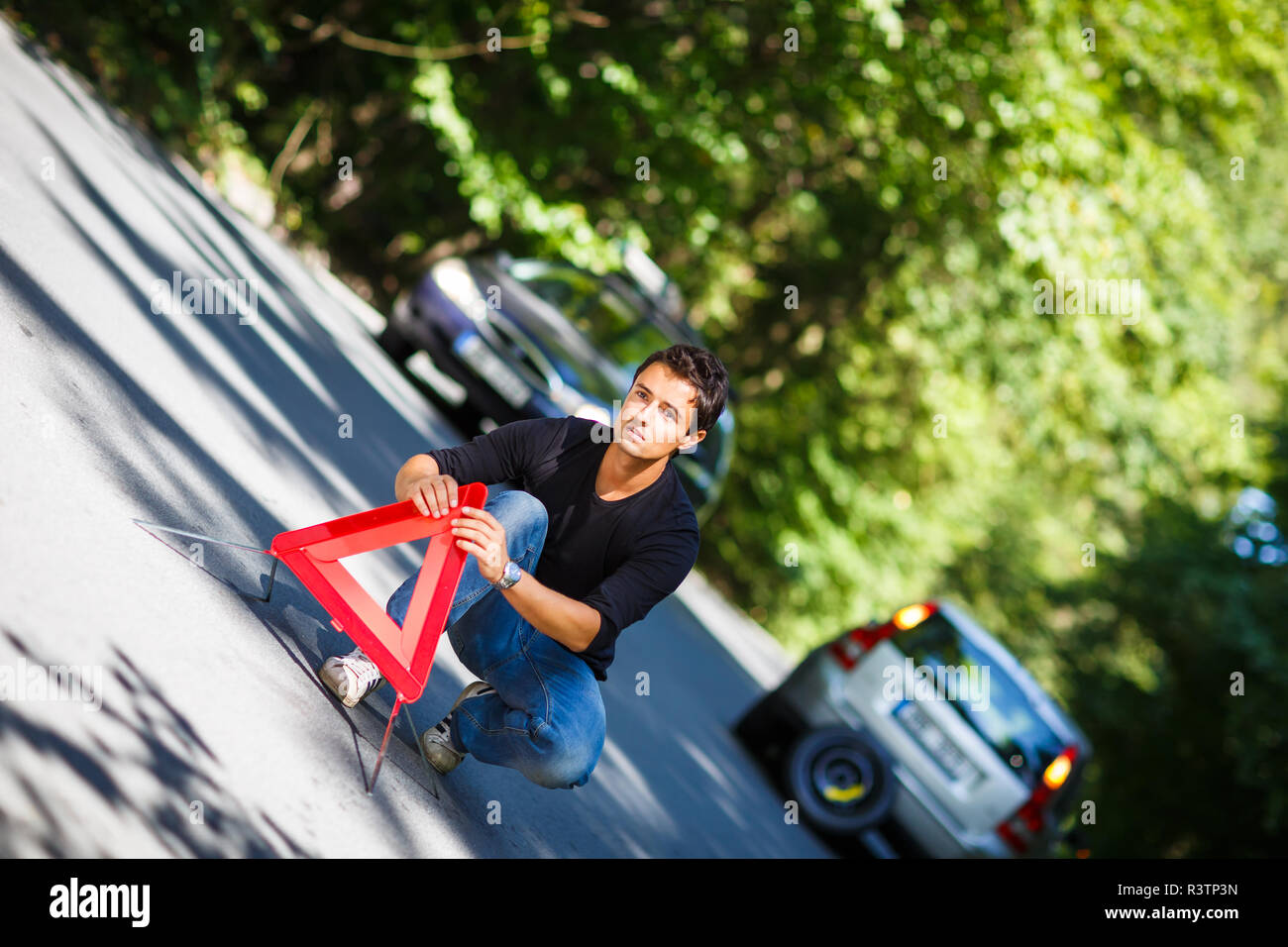 Bel giovane uomo con la sua vettura ripartiti per la strada, l'impostazione del triangolo di sicurezza Foto Stock