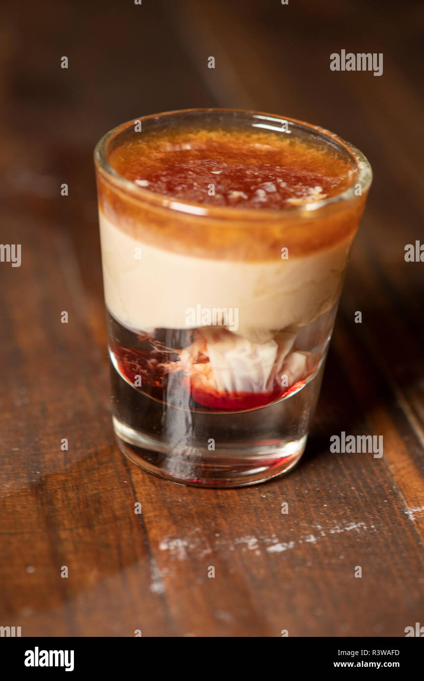 Emorragia cerebrale shot cocktail con schnapps, baileys Irish cream e grenadine con uno sfondo di legno Foto Stock