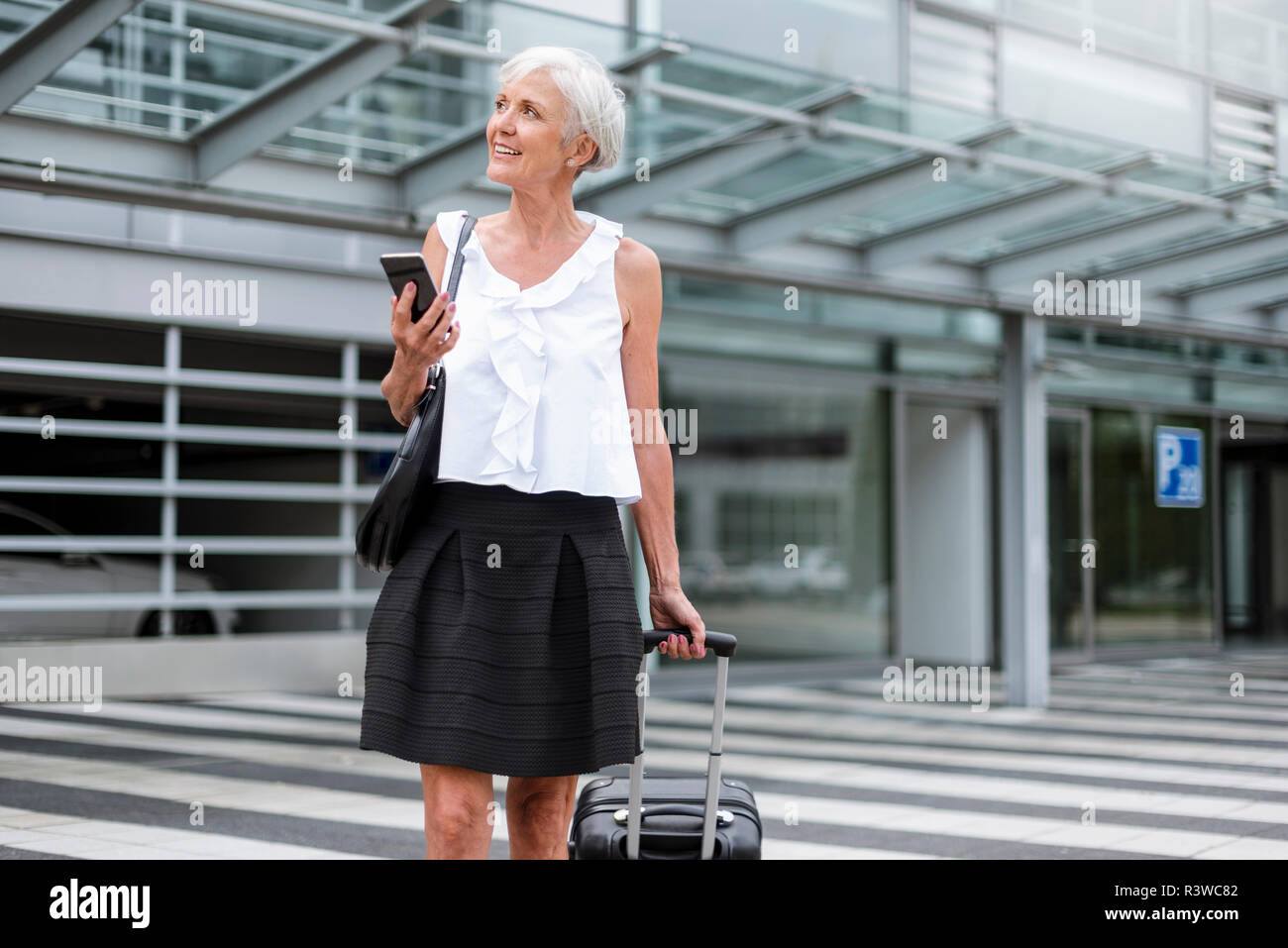 Sorridente donna senior con un telefono cellulare e il bagaglio in movimento Foto Stock
