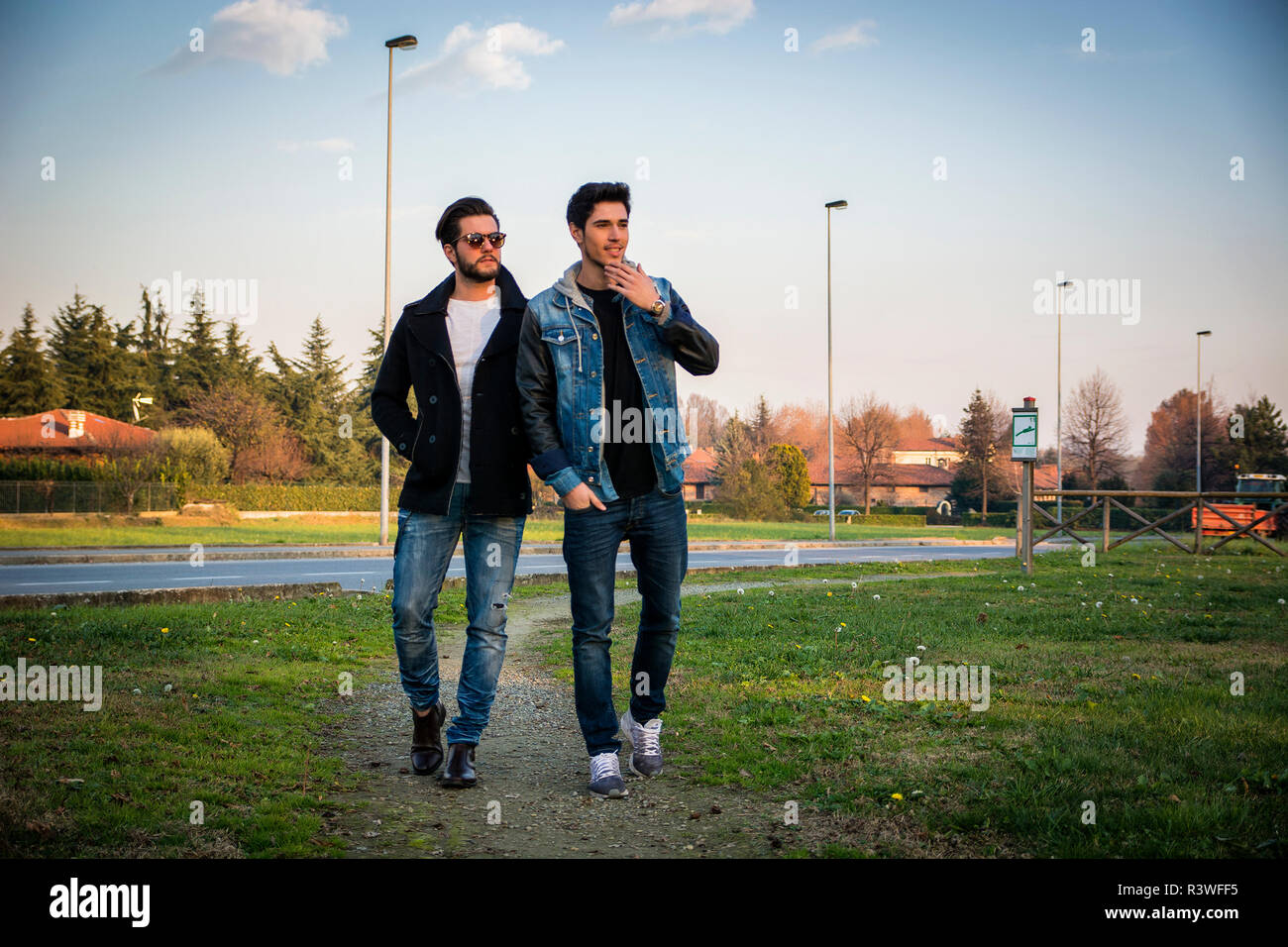 Due graziosi alla moda casual giovani uomini, 2 amici, in un parco urbano a piedi e chiacchierare insieme Foto Stock