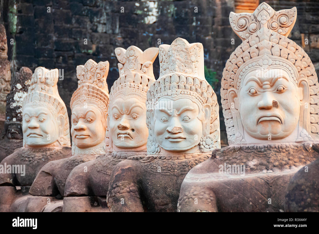 Demoni di pietra (asuras) linea una strada rialzata che conduce a Angkor Thom mostrando i 'demoni' che portano headdress militare - Siem Reap, Cambogia, Sud-Est asiatico Foto Stock