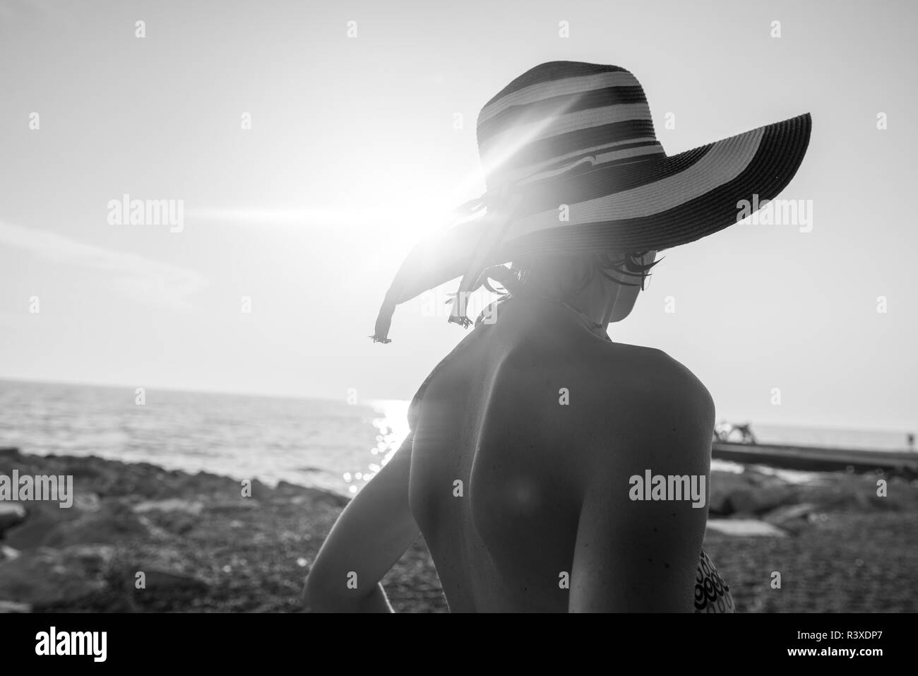 Immagine monocromatica di donna presso la spiaggia per guardare il tramonto sull'oceano con un sole luminoso flare da dietro. Foto Stock