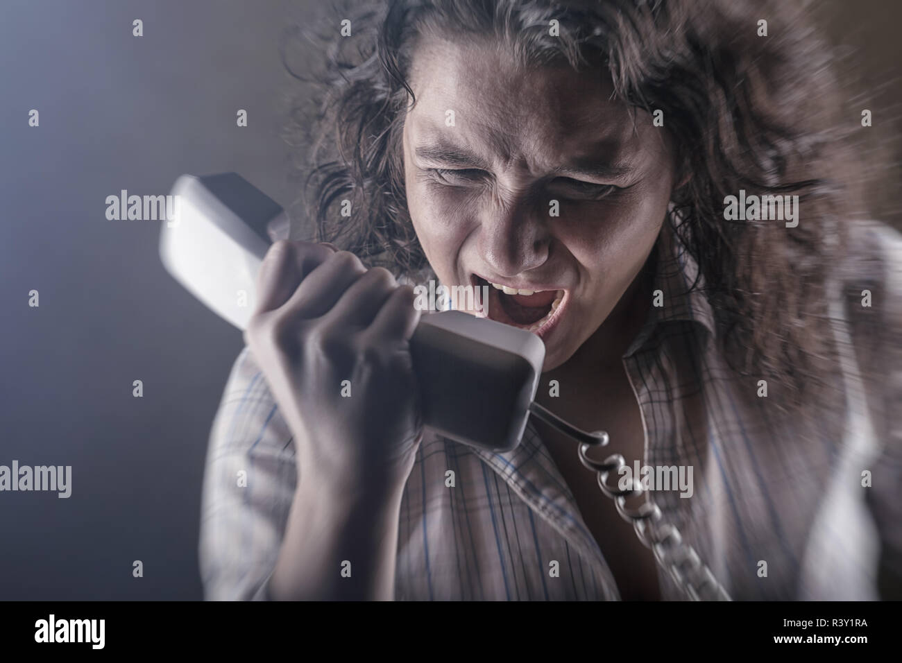 Giovane donna arrabbiato urlando nel telefono su sfondo scuro Foto Stock