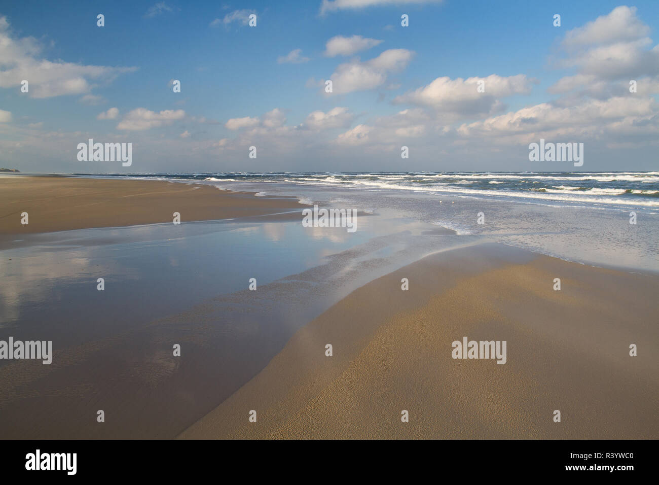 Vasta spiaggia di marea di declino, cielo blu e nuvole bianche si riflette nell'acqua di un burrone Foto Stock