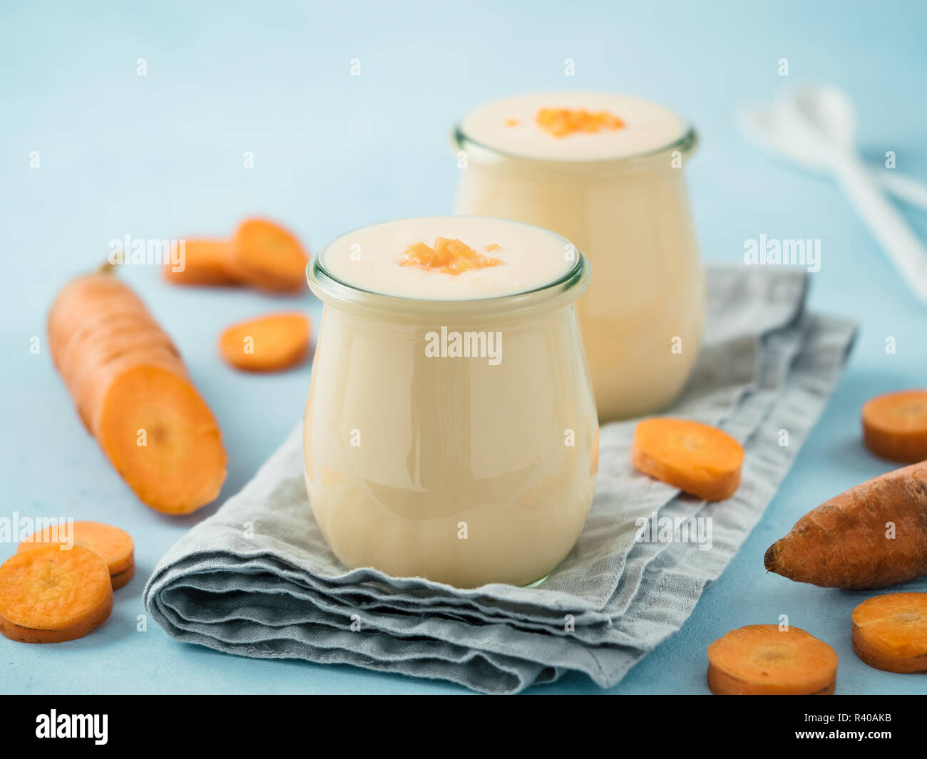 Yogurt con la carota. Yogurt vegetale. 2 vasetto di vetro con giallo arancione yogurt o frullato e carota fresca su sfondo blu. Copia spazio per il testo Foto Stock
