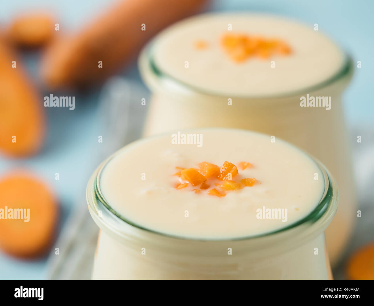 Yogurt con la carota. Yogurt vegetale. 2 vasetto di vetro con giallo arancione yogurt o frullato e carota fresca su sfondo blu. Copia spazio per il testo Foto Stock
