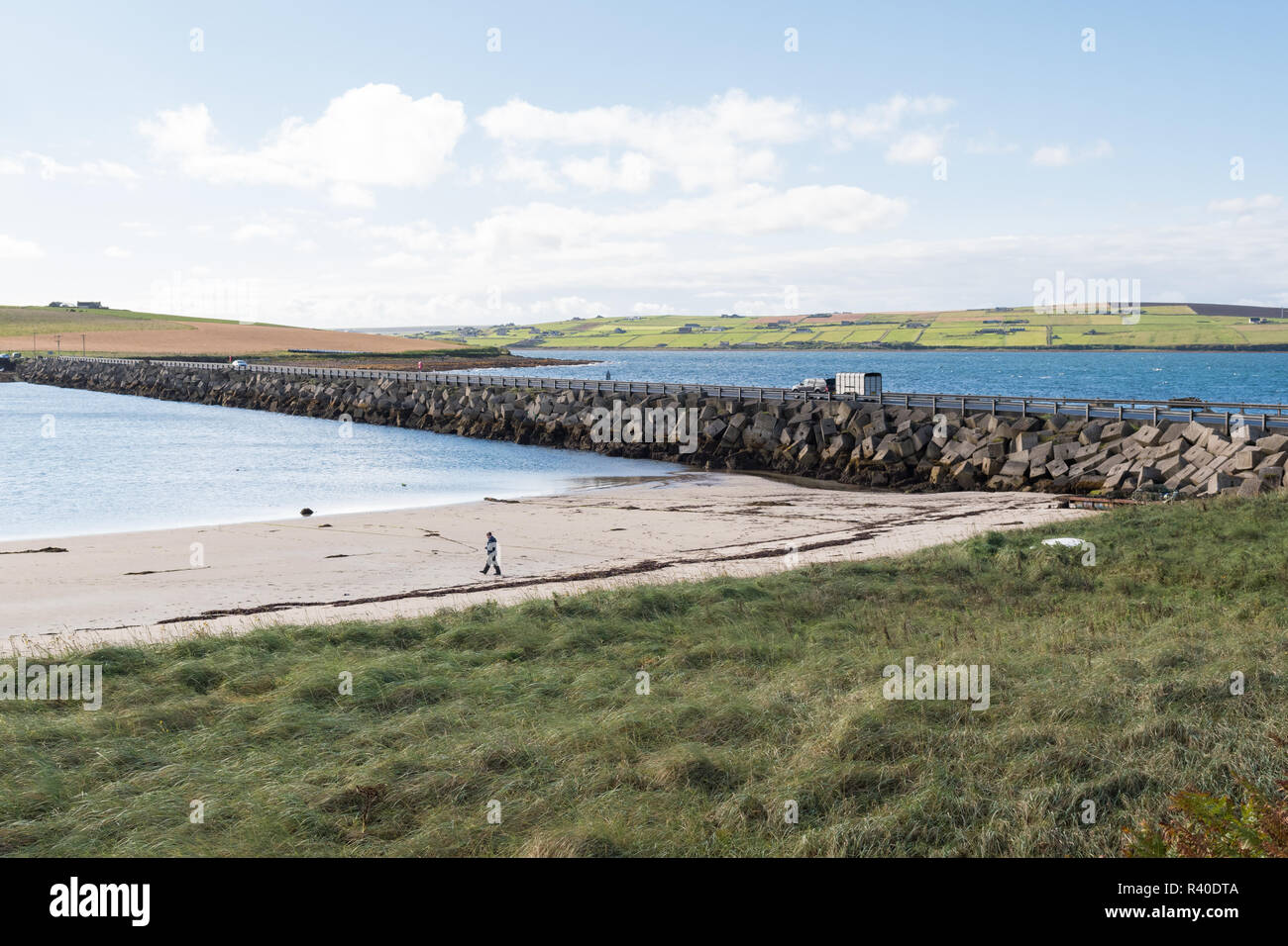 Uomo a camminare sulla spiaggia accanto alla barriera di Churchill n. 3 causeway, collegando le isole di Vi riportiamo Holm e Burray, , le Orcadi Scozia, Regno Unito Foto Stock