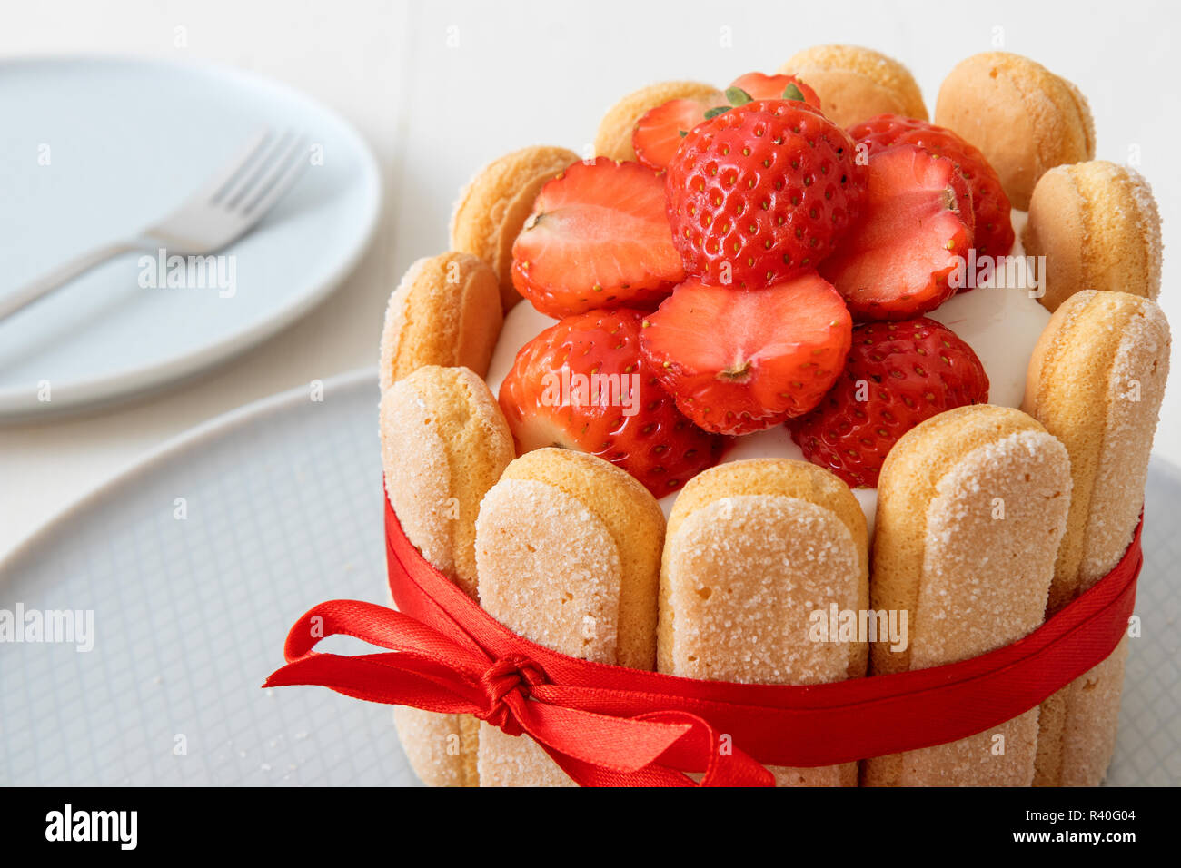 Charlotte, francese dessert con fragole, legato con un nastro rosso scarlatto, tazza di caffè, la ciotola con le fragole sul tavolo bianco. Foto Stock