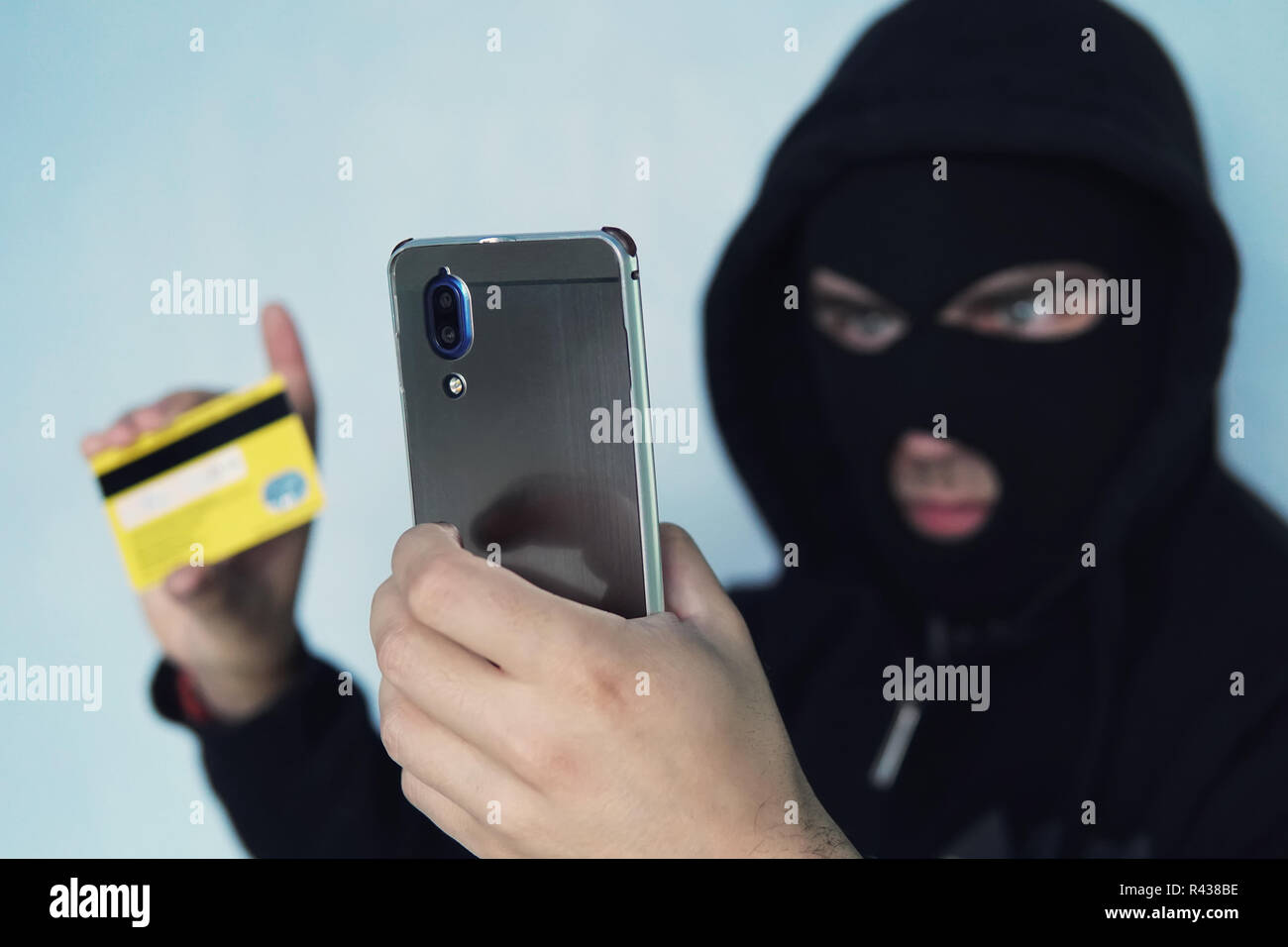 Il ladro scammer è in possesso di un telefono cellulare e una carta di credito. Il concetto di banca di frode della carta di credito attraverso un virus nello smartphone. un delinquente in un nero Balac Foto Stock