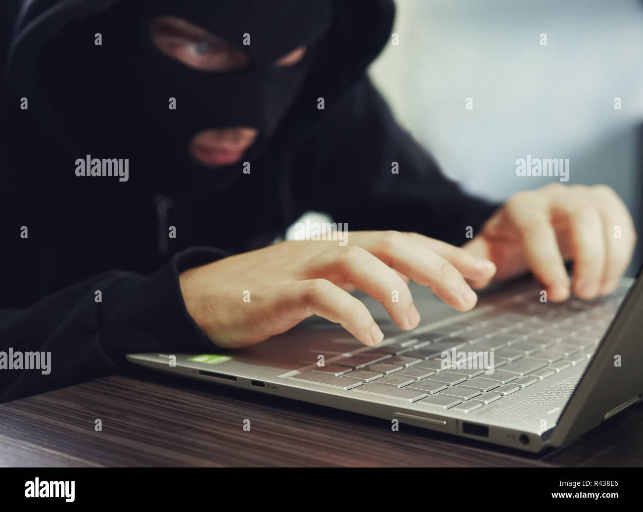 Close up di un mal intenzionato hacker in nero balaclava immettendo i dati su un computer portatile. Hacker commette reati informatici. Un uomo seduto con nascosto Foto Stock