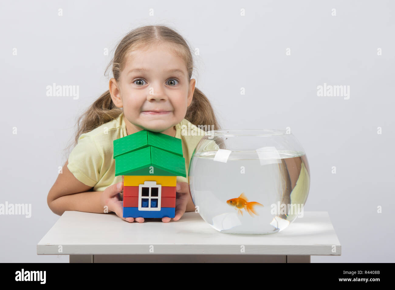 Quattro anni di ragazza con un giocattolo di casa e si siede di fronte a un goldfish Foto Stock