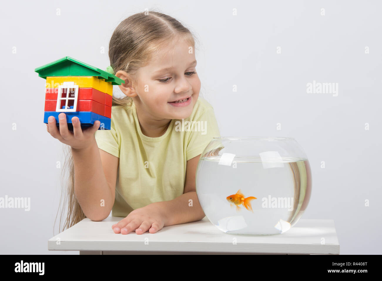 Quattro anni di ragazza si siede con un giocattolo di casa nella parte anteriore di un goldfish Foto Stock