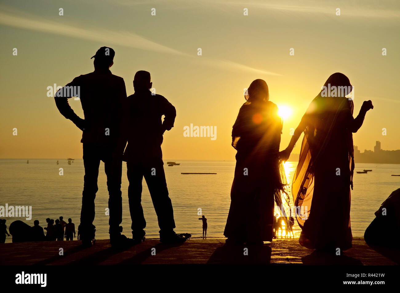 Tramonto a Marine Drive presso l'Oceano Indiano, a Mumbai, India, due coppie indiane in piedi sulla parete argine che appaiono ma come silhouette Foto Stock