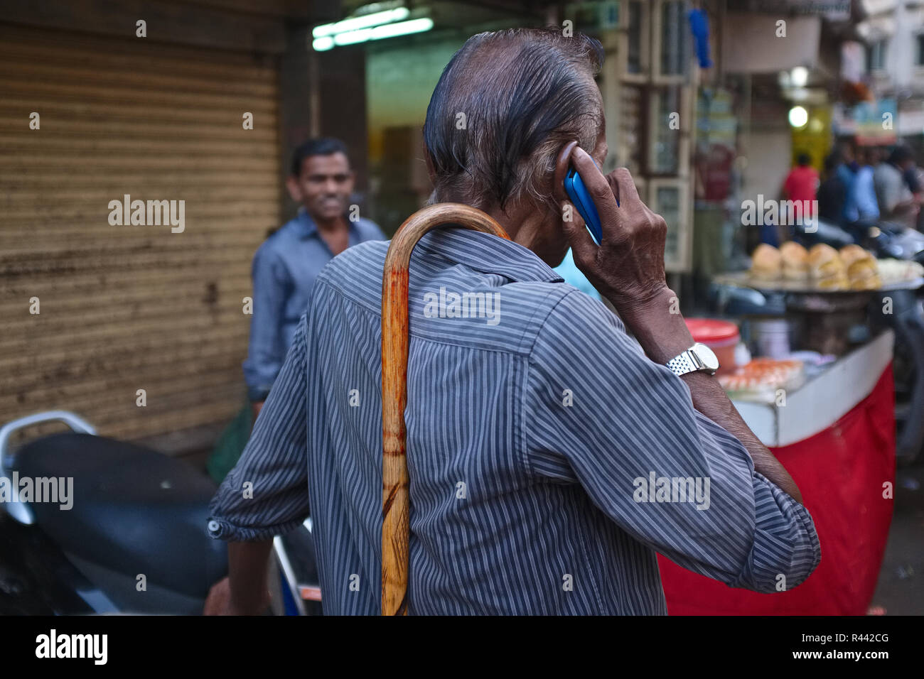 Mani libere: un utente mobile in una area di mercato in Mumbai, India, avendo trovato un modo intelligente per portare il suo bastone da passeggio quando non è in uso Foto Stock