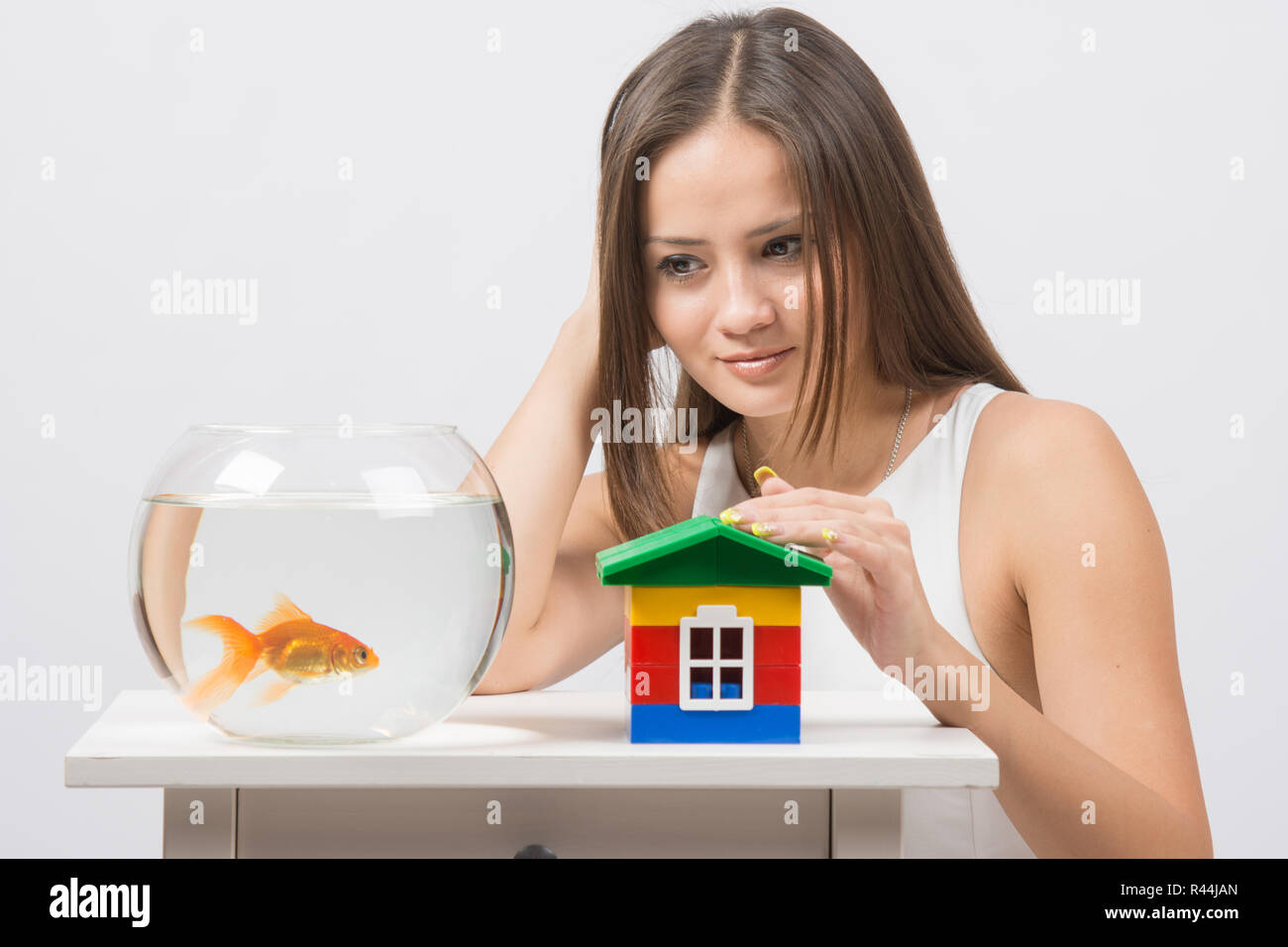 La ragazza guarda un goldfish e mettere la mano sul giocattolo house Foto Stock