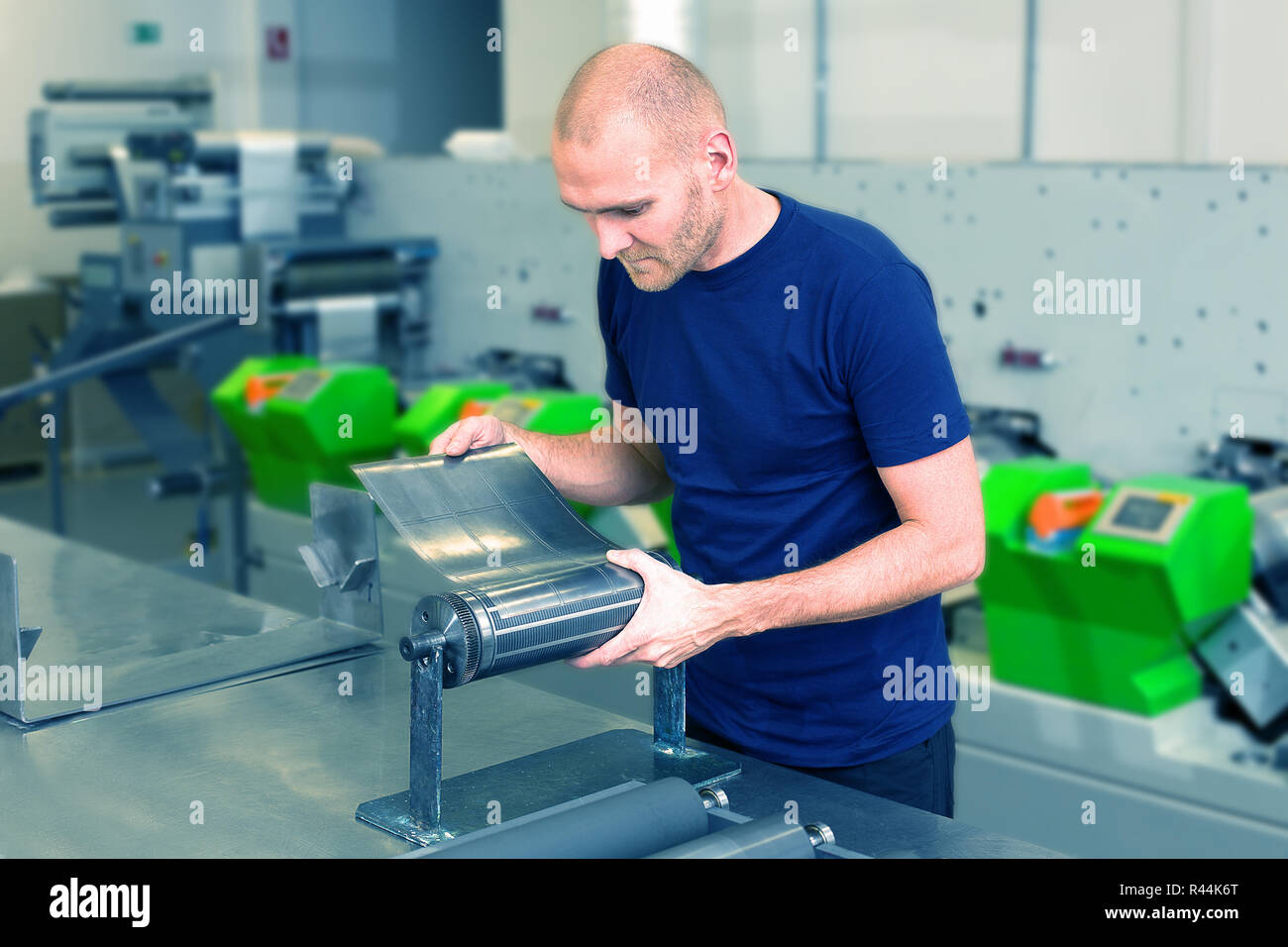 Flexo di taglio a stampo rotante preparazione. Lavoratore nella stampa di fabbrica, in piedi accanto alla macchina da stampa la preparazione di matrice cilindrica. Operatore allinea tagliare Foto Stock