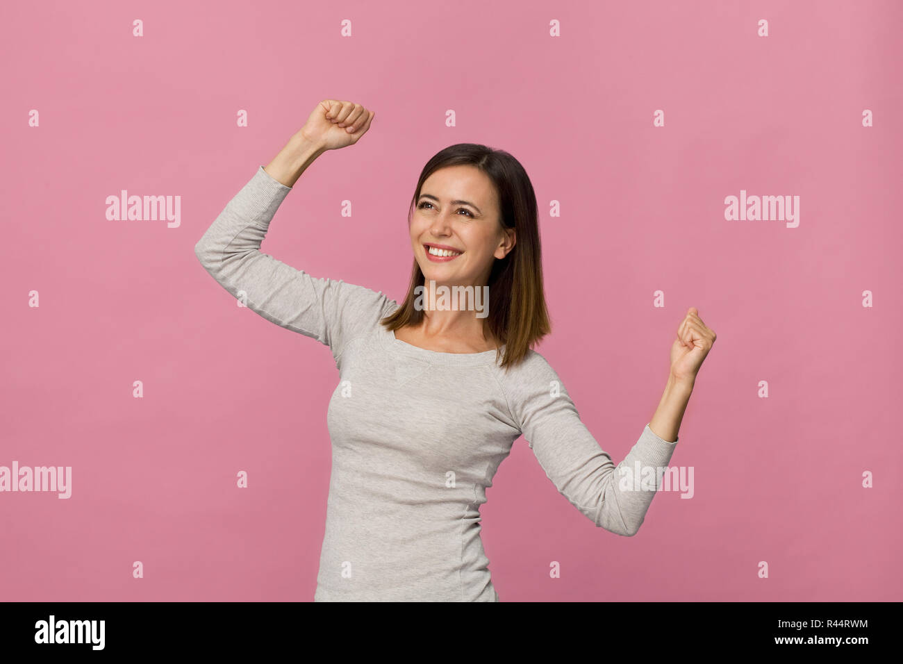 Felice bruna giovane donna sorridente ritratto gesto di vittoria contro sfondo rosa Foto Stock