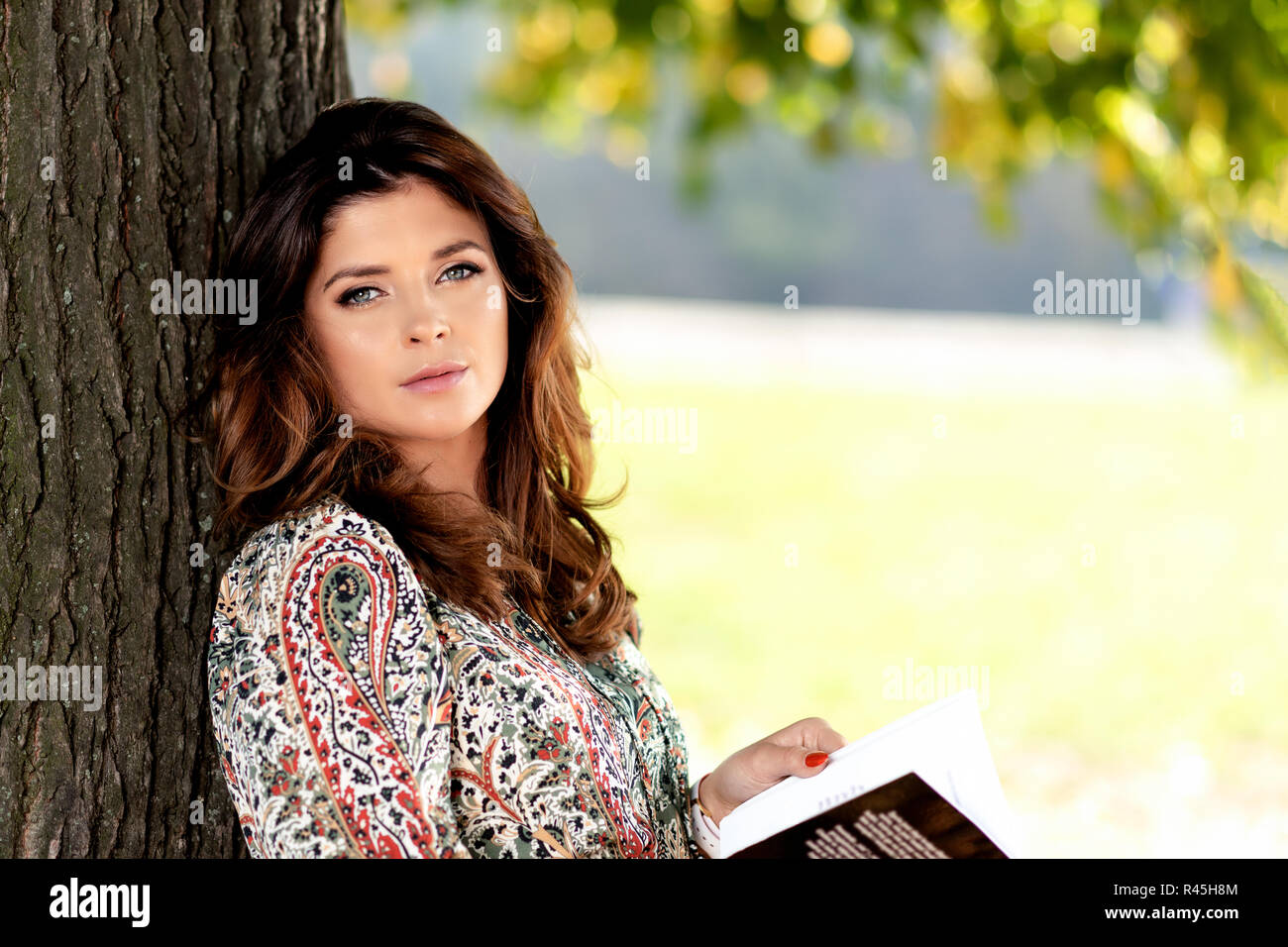 Ritratto di una sensuale e bella donna con una bella acconciatura libro lettura all'aperto in una giornata di sole sotto l'albero ( copia spazio) Foto Stock