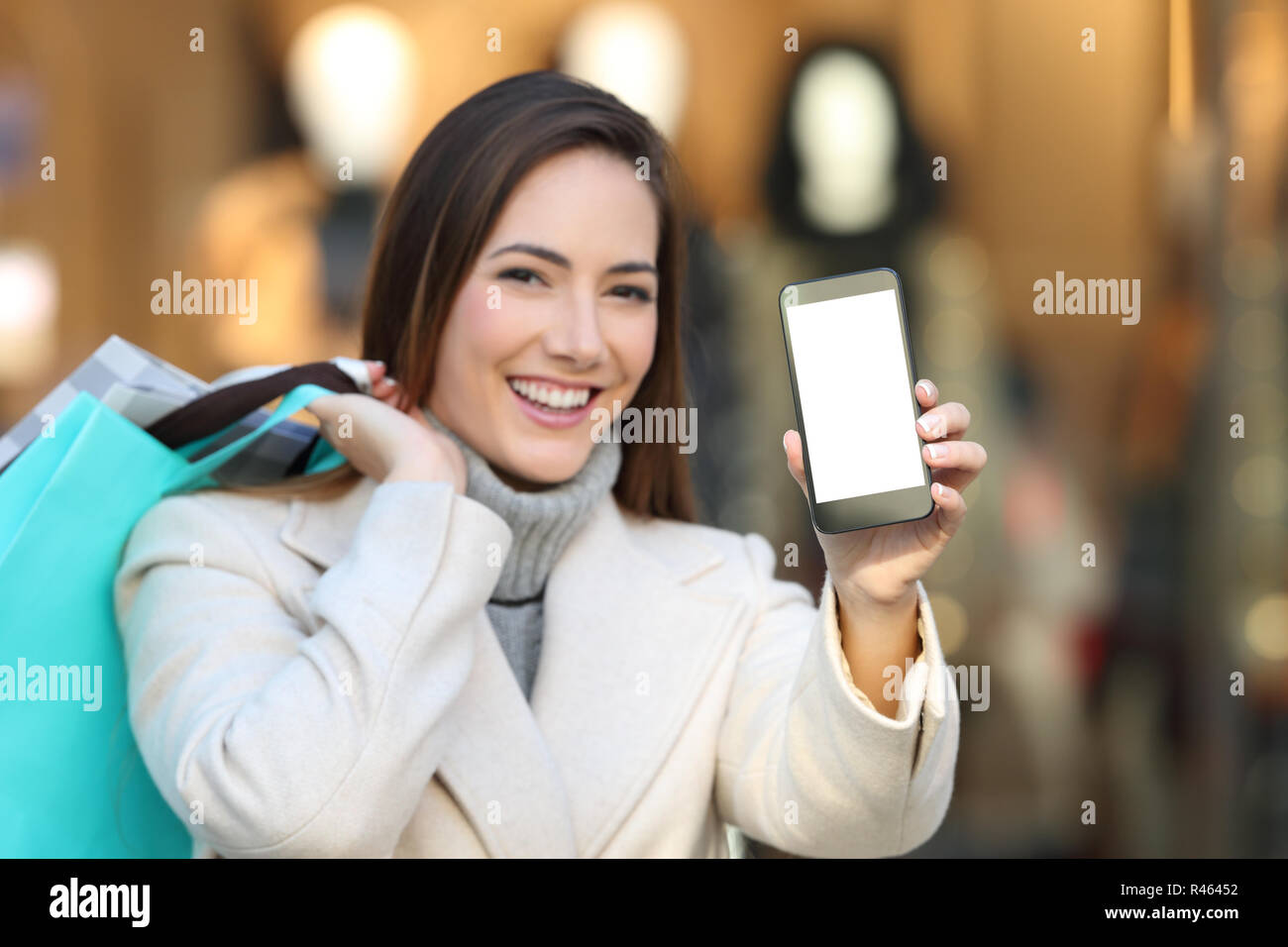 Felice Tiene shopper shopping bags mostra vuoto smart Schermata telefono in inverno in un centro commerciale Foto Stock