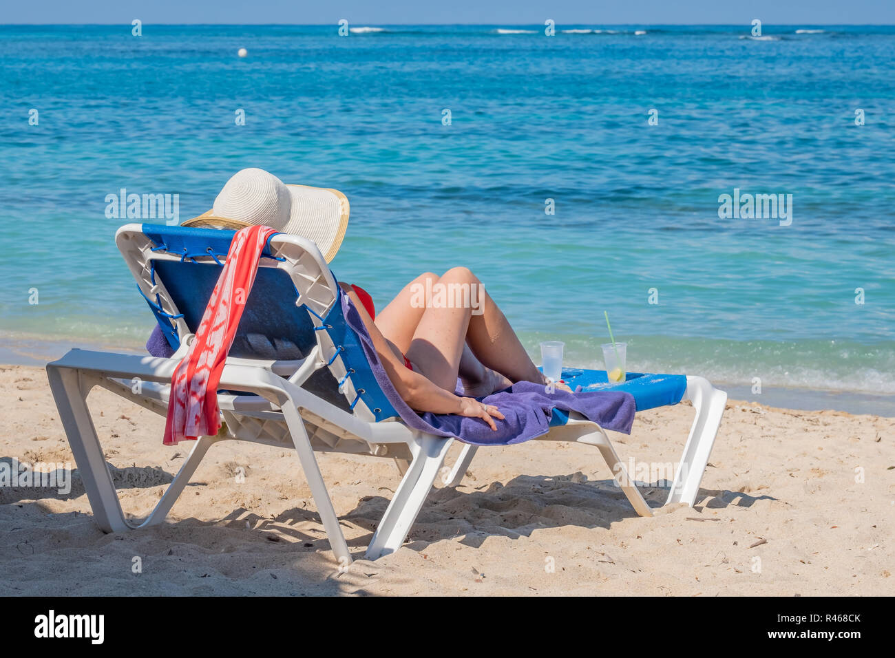 Caucasion donna che indossa un cappello di paglia seduto in una sedia a sdraio in Playa Jibacoa sulla costa atlantica di Cuba. Foto Stock