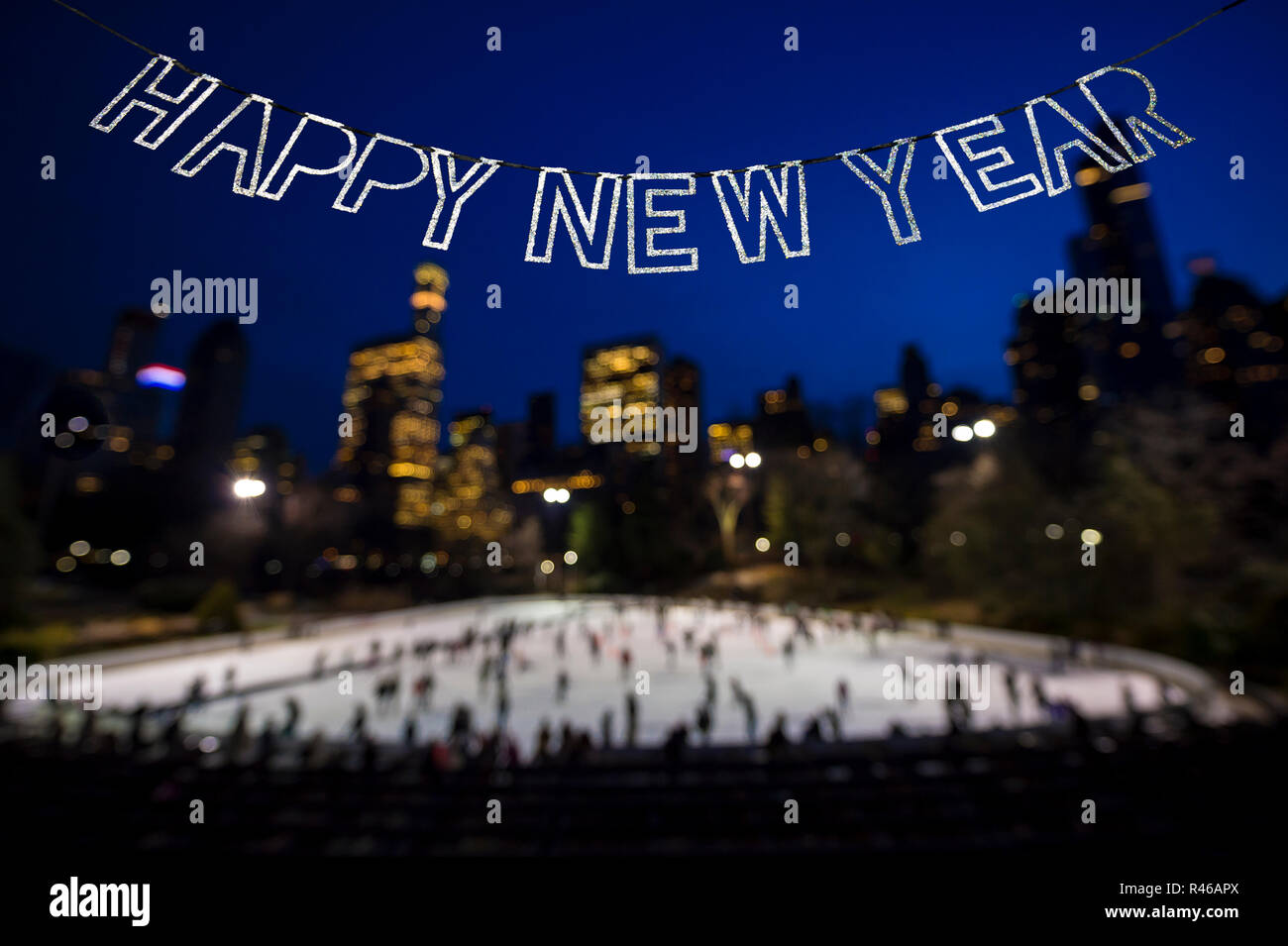 Felice Anno Nuovo messaggio in shiny bunting appeso nel cielo invernale al di sopra di un occupato il pattinaggio su ghiaccio circondato da scintillanti luci della città Foto Stock