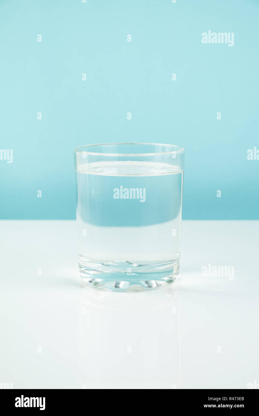 Vetro con acqua su una tabella. La fame o la dieta concetto: pulire transparrent bere in bianco e lo sfondo blu Foto Stock