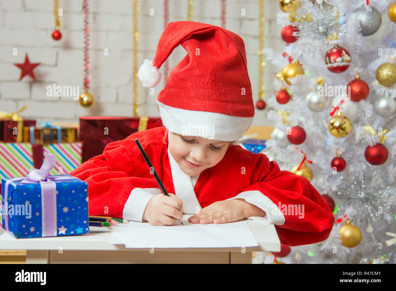 Ragazza vestita come Santa Claus scrivere un elenco di desiderata di regali di Natale Foto Stock