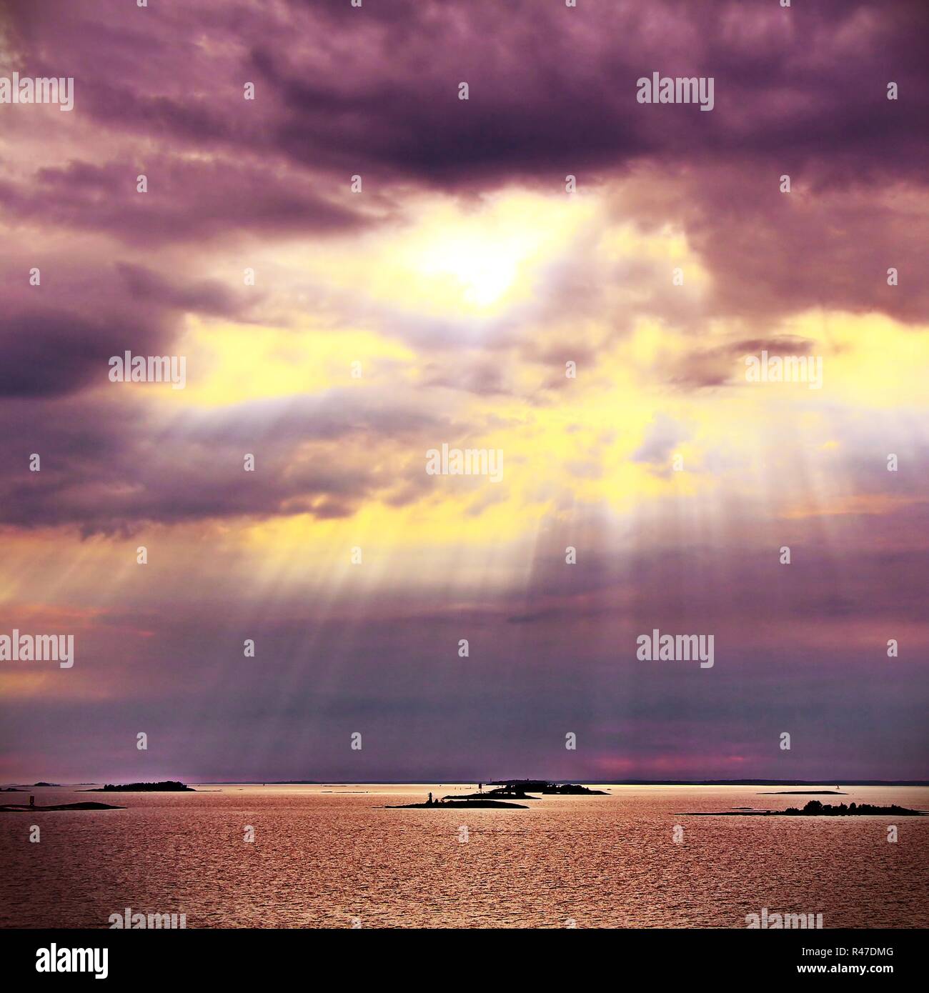 Il sole dietro le nuvole con i raggi di luce che risplende in giù sul mare Foto Stock