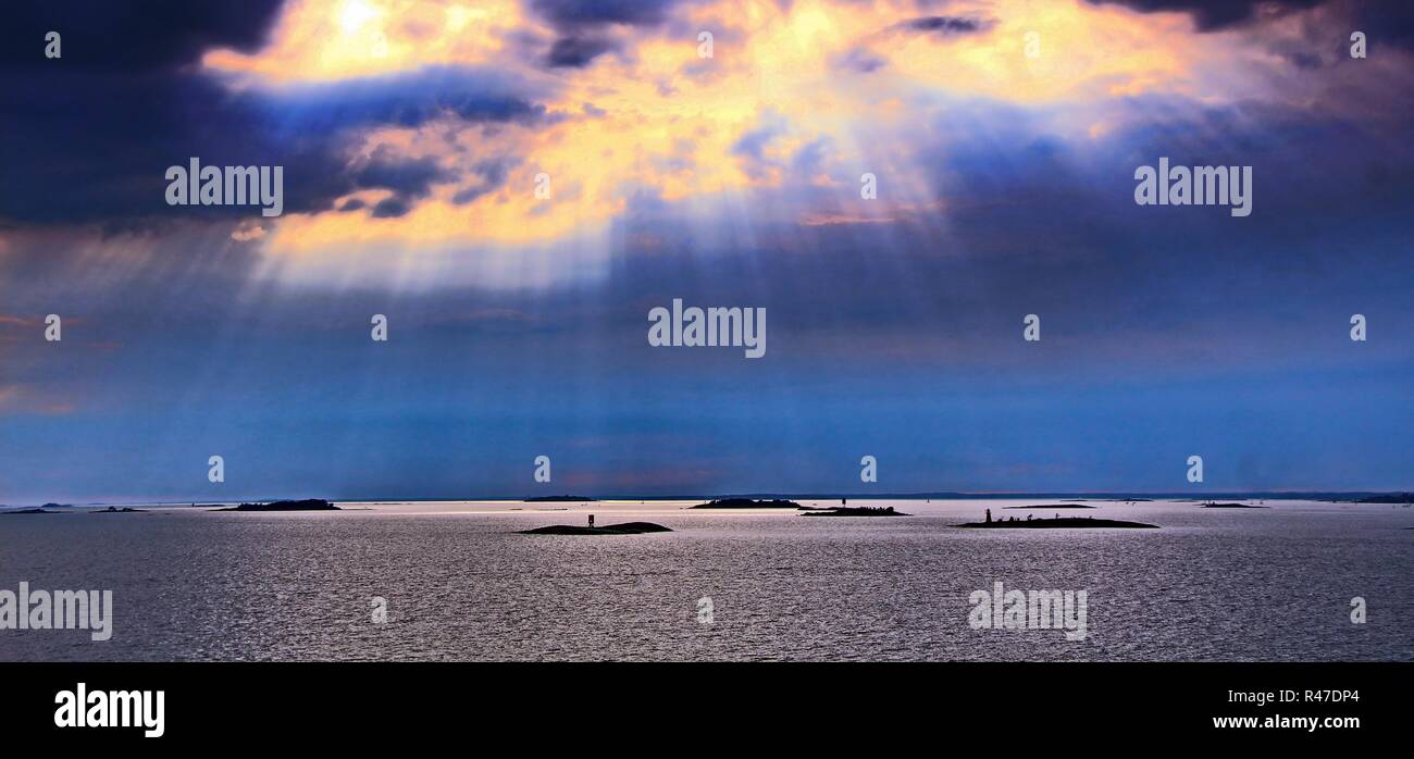 Il sole dietro le nuvole con i raggi di luce che risplende in giù sul mare Foto Stock