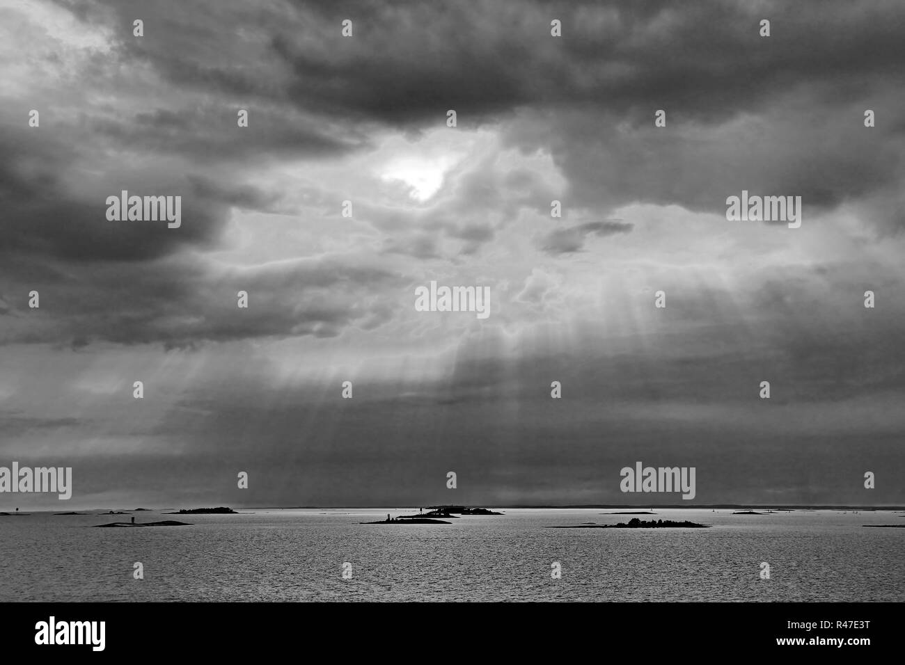 Il sole dietro le nuvole con i raggi di luce che risplende in giù sul mare Foto Stock