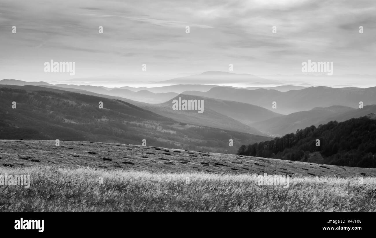Incredibile visualizzazione bianco e nero di forme di infinite, morbido, misty strati di montagna, erba in primo piano e cielo drammatico Foto Stock