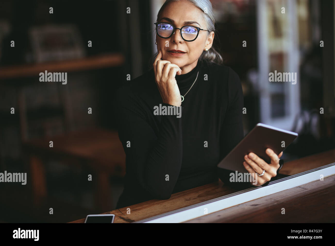 Senior imprenditrice seduti ad un tavolo da caffè con tavoletta digitale. Donna matura in un momento di relax a un ristorante con i tablet pc. Foto Stock